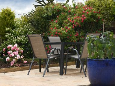A patio with a black table and four chairs surrounded by flowering bushes and a blue pot plant at Summerfold in Warkworth