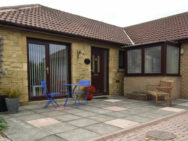 A patio with blue table and chairs a wooden bench and stone house exterior at Summerfold in Warkworth