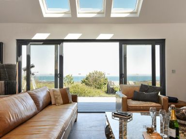 A living room with leather sofas a telescope and sliding glass doors with a sea view at Waters Edge Beadnell Harbour Road in Beadnell