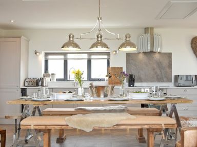A kitchen with a wooden dining table set with plates glasses and flowers at Waters Edge Beadnell (Harbour Road) in Beadnell