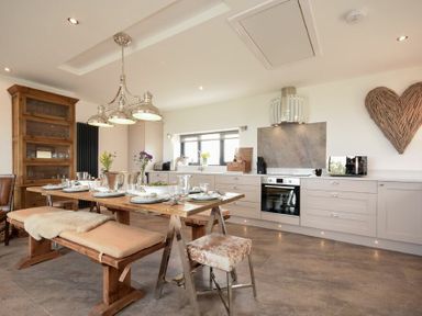 A kitchen with a wooden dining table set with plates and glasses benches and stools cabinets and appliances on one side at Waters Edge Beadnell Harbour Road in Beadnell