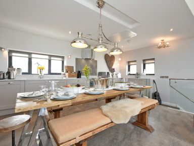 A dining area with a wooden table set for six and a kitchen area with gray cabinets at Waters Edge Beadnell Harbour Road in Beadnell