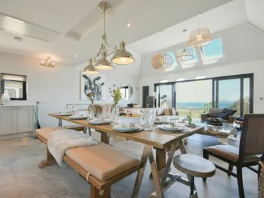 A dining area with a wooden table set for a meal including plates and glasses and a living area with sofas and large windows showing a sea view at Waters Edge Beadnell (Harbour Road) in Beadnell