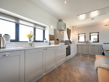A kitchen with gray cabinets and countertop with a built-in oven and a window at Waters Edge Beadnell (Harbour Road) in Beadnell