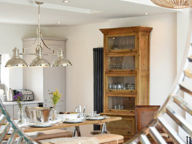 A dining area with a wooden table set with plates and glasses next to a wooden cabinet with glass doors at Waters Edge Beadnell Harbour Road in Beadnell