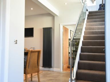 A staircase with carpet and glass railing next to a dining area with wicker chairs and a wall-mounted radiator at Waters Edge Beadnell Harbour Road in Beadnell