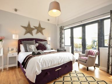 A bedroom with a bed pillows armchair rug and large windows at Waters Edge Beadnell Harbour Road in Beadnell