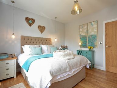 A bedroom with a bed pillows and blankets bedside tables with lamps and a chest of drawers with flowers at Waters Edge Beadnell Harbour Road in Beadnell