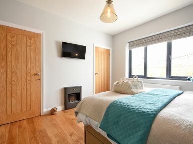 A bedroom with a bed with blankets a wall-mounted tv a small fireplace wooden doors and a window at Waters Edge Beadnell Harbour Road in Beadnell