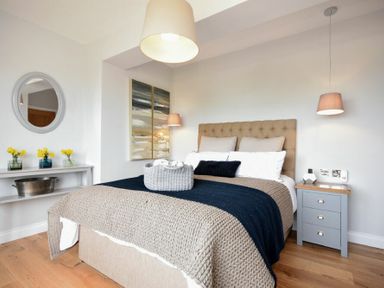A bedroom with a bed a bedside table with lamps and flowers on a shelf at Waters Edge Beadnell Harbour Road in Beadnell