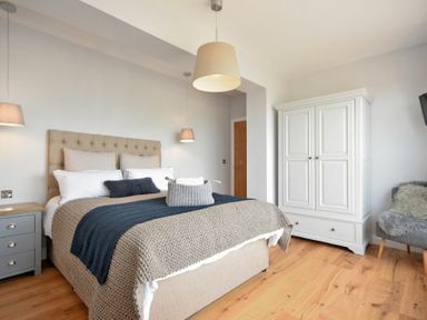 A bedroom with a bed and bedside table next to a white wardrobe and a chair at Waters Edge Beadnell (Harbour Road) in Beadnell