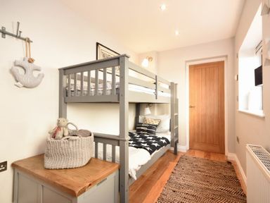 A bedroom with a gray bunk bed a wooden door and a wicker basket on a cabinet at Waters Edge Beadnell Harbour Road in Beadnell