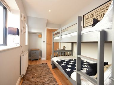 A bedroom with a bunk bed a rug on the floor and a small chest of drawers at Waters Edge Beadnell (Harbour Road) in Beadnell