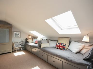 A room with built in bench seating under skylights and pillows next to a wooden chair and cabinet at Waters Edge Beadnell Harbour Road in Beadnell