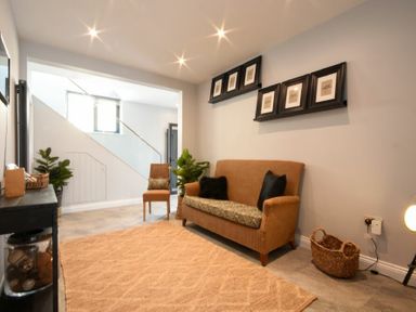 A sitting room with a sofa, chair, wall shelves with picture frames, plants, and a rug at Waters Edge Beadnell (Harbour Road) in Beadnell