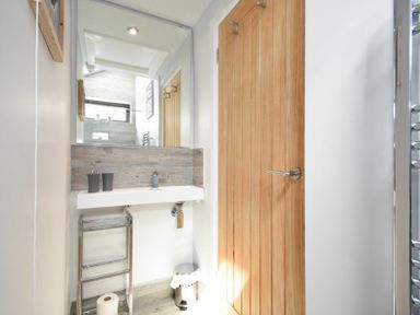 A bathroom with a sink mirror wooden door and metal towel rack at Waters Edge Beadnell Harbour Road in Beadnell