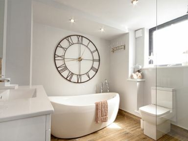 A bathroom with a freestanding bathtub a large wall clock a toilet and a window at Waters Edge Beadnell Harbour Road in Beadnell