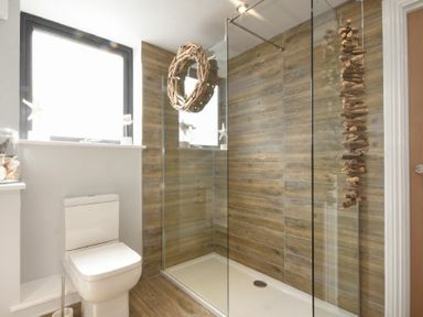 A bathroom with a toilet and a walk in shower with glass panel and wooden wall tiles at Waters Edge Beadnell (Harbour Road) in Beadnell