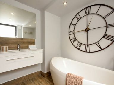 A bathroom with a white bathtub a large clock on the wall and a white sink with a mirror at Waters Edge Beadnell Harbour Road in Beadnell