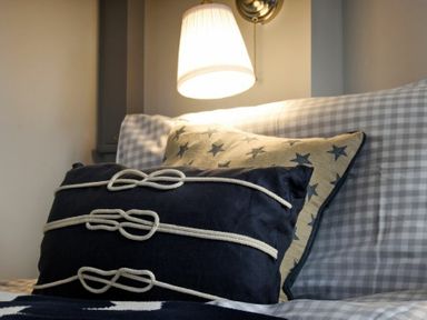 A sofa with star patterned cushions and a lit wall lamp above at Waters Edge Beadnell (Harbour Road) in Beadnell