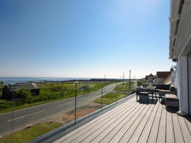 A balcony with outdoor furniture overlooking a road and the sea at Waters Edge Beadnell Harbour Road in Beadnell