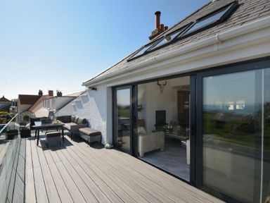An outdoor deck with seating furniture and a table next to large glass sliding doors at Waters Edge Beadnell Harbour Road in Beadnell