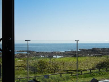 A glass balcony overlooking grass shrubs rocky shore and sea at Waters Edge Beadnell Harbour Road in Beadnell