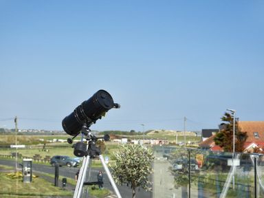 A telescope on a tripod on a balcony with road and houses in the background at Waters Edge Beadnell Harbour Road in Beadnell
