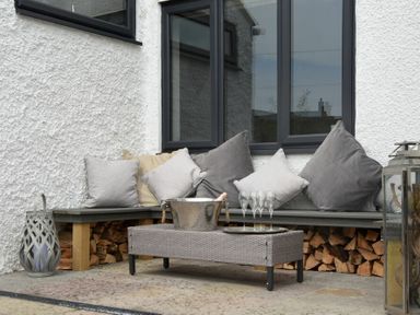 An outdoor seating area with cushions on a wooden bench and a table with glasses and an ice bucket at Waters Edge Beadnell Harbour Road in Beadnell