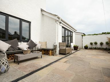 An outdoor patio area with cushioned bench seating wooden firewood and potted plants at Waters Edge Beadnell Harbour Road in Beadnell