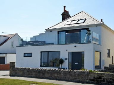 A two-story house with glass balcony and stone wall in front at Waters Edge Beadnell Harbour Road in Beadnell