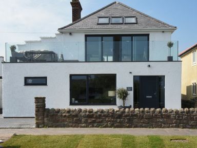 A two story house with white exterior walls and black framed windows and doors with a stone wall in front at Waters Edge Beadnell Harbour Road Beadnell