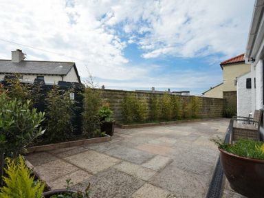 A paved outdoor patio area with plants along a brick wall and garden furniture at Waters Edge Beadnell Harbour Road in Beadnell