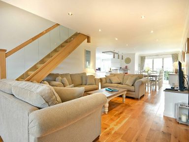 A living room with beige sofas a wooden coffee table a TV stand and a staircase with glass panels at Portland in Beadnell