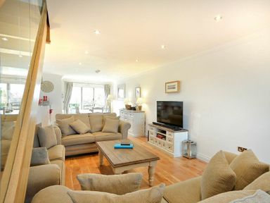 A living room with beige sofas a wooden coffee table a TV on a white stand and dining area visible at Portland in Beadnell