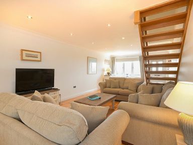 A living room with beige sofas a wooden coffee table a television and wooden stairs at Portland in Beadnell