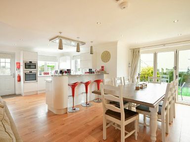 A kitchen and dining area with white cabinets red bar stools and a wooden dining table at Portland in Beadnell