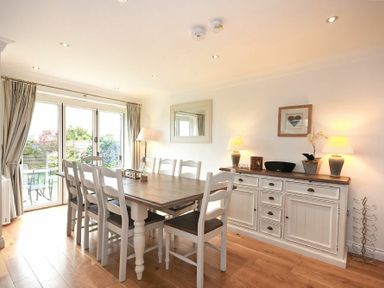 A dining room with a wooden table and eight chairs next to a cabinet with lamps and a framed picture at Portland in Beadnell