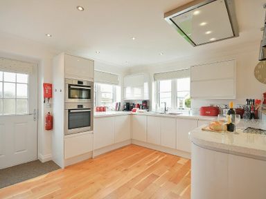 A kitchen with white cabinets built-in oven coffee makers and a wooden floor at Portland in Beadnell