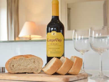 A bottle of wine with three wine glasses and sliced bread on a cutting board