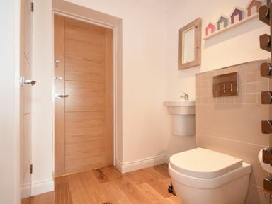 A bathroom with a wooden door a white toilet a small sink a mirror and decorative house figures on a shelf at Portland in Beadnell