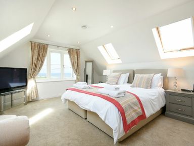 A bedroom with a double bed bedside tables a television and windows with curtains at Portland in Beadnell