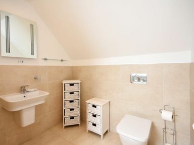 A bathroom with a wall-mounted sink a mirror two storage units a toilet and a toilet paper holder at Portland in Beadnell