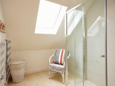 A bathroom with a wicker chair with a striped cushion a wicker laundry basket a glass shower enclosure and a skylight roof window at Portland in Beadnell