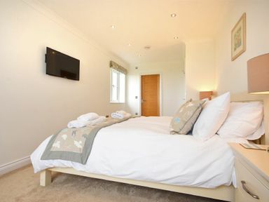 A bedroom with a bed with pillows and folded towels a wall mounted television and a wooden door in Portland Beadnell