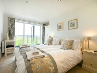 A bedroom with a double bed pillows and folded towels near a large glass door with curtains at Portland in Beadnell