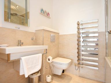 A bathroom with a wall-mounted sink and towel rack a toilet with a toilet paper holder a chrome heated towel rail and a mirror at Portland in Beadnell