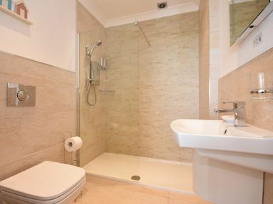 A bathroom with a shower area a wall-mounted toilet and a sink at Portland in Beadnell