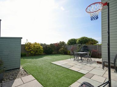 A backyard with artificial grass a basketball hoop a patio with a table and chairs and a shed at Portland in Beadnell
