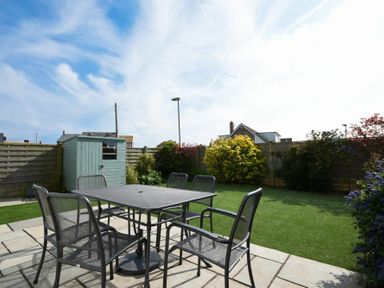 A garden with a metal table and six chairs on a paved patio with a shed and plants at Portland in Beadnell